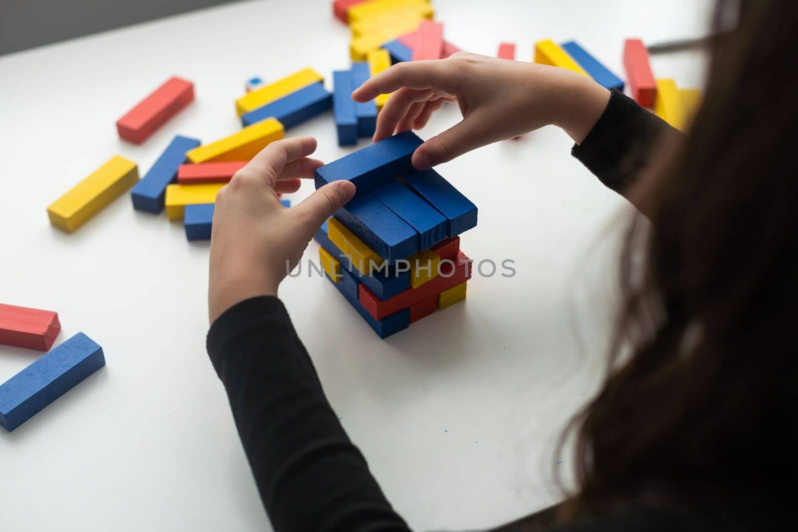 a little happy girl is playing the board game at the table. Construction of a tower made of wooden cubes by Andelov13