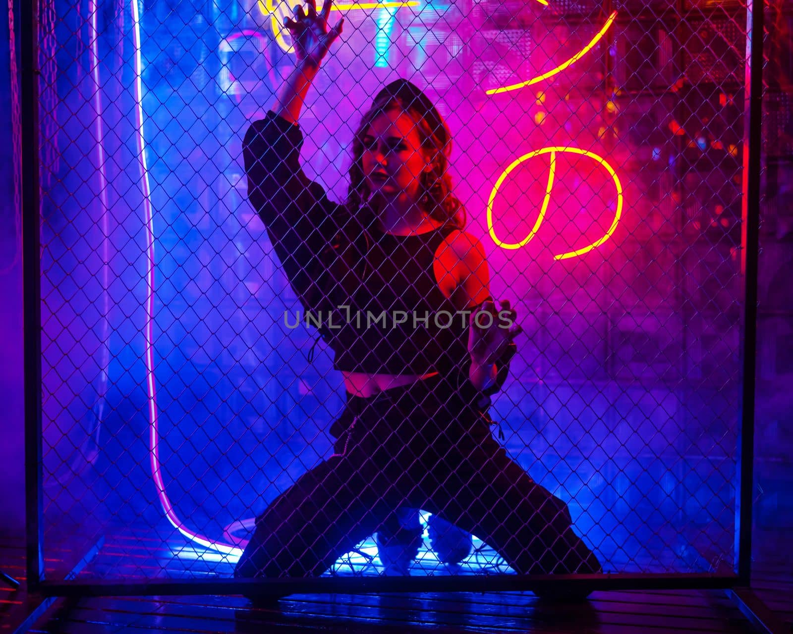 Caucasian woman in neon studio behind chain-link mesh