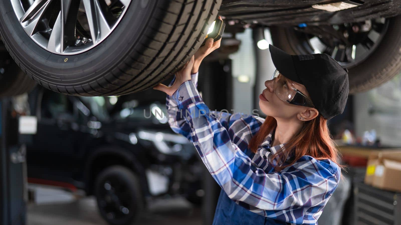 A female mechanic inspects a raised car. A girl at a man's work