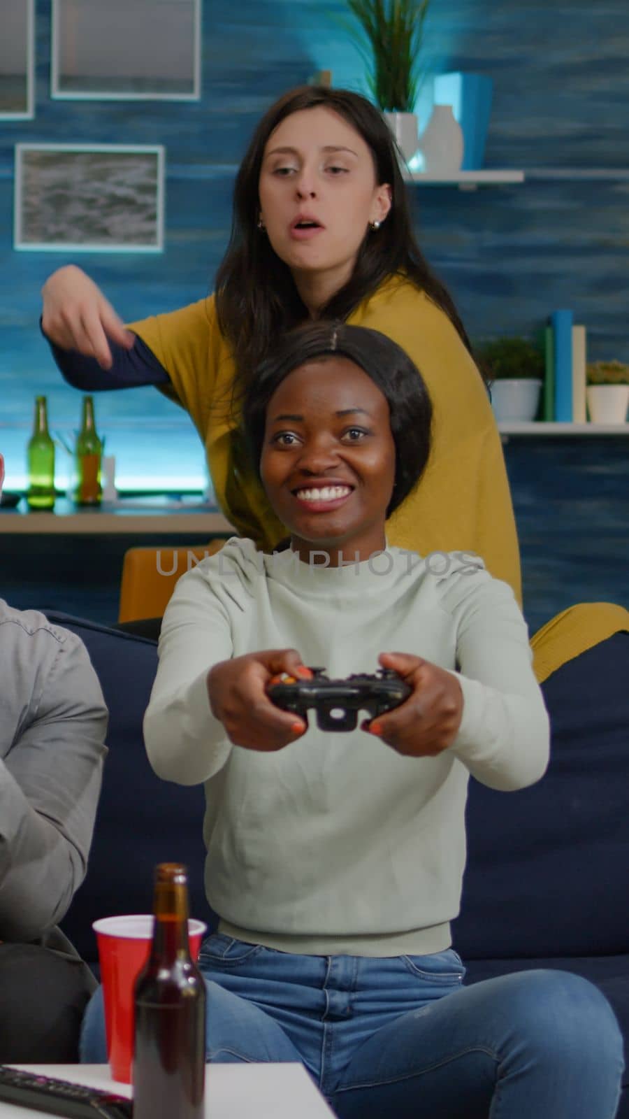 Woman with blak skin playing online videogames against man friends during competition simulation using controller. Group of mixed race winning game while sitting on sofa in living room late at night