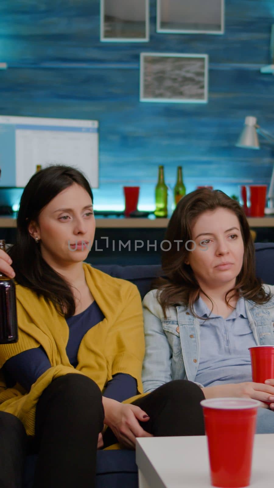 Group of mixed race friends relaxing on sofa while watching entertainment movie on television laughting late at living room during home party. Group of multi-ethnic people enjoying time together