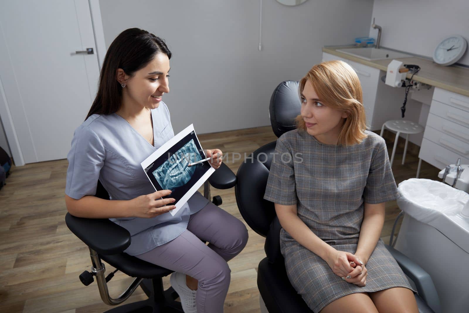 Female dentist pointing at patient's X-ray image in dental office by Mariakray