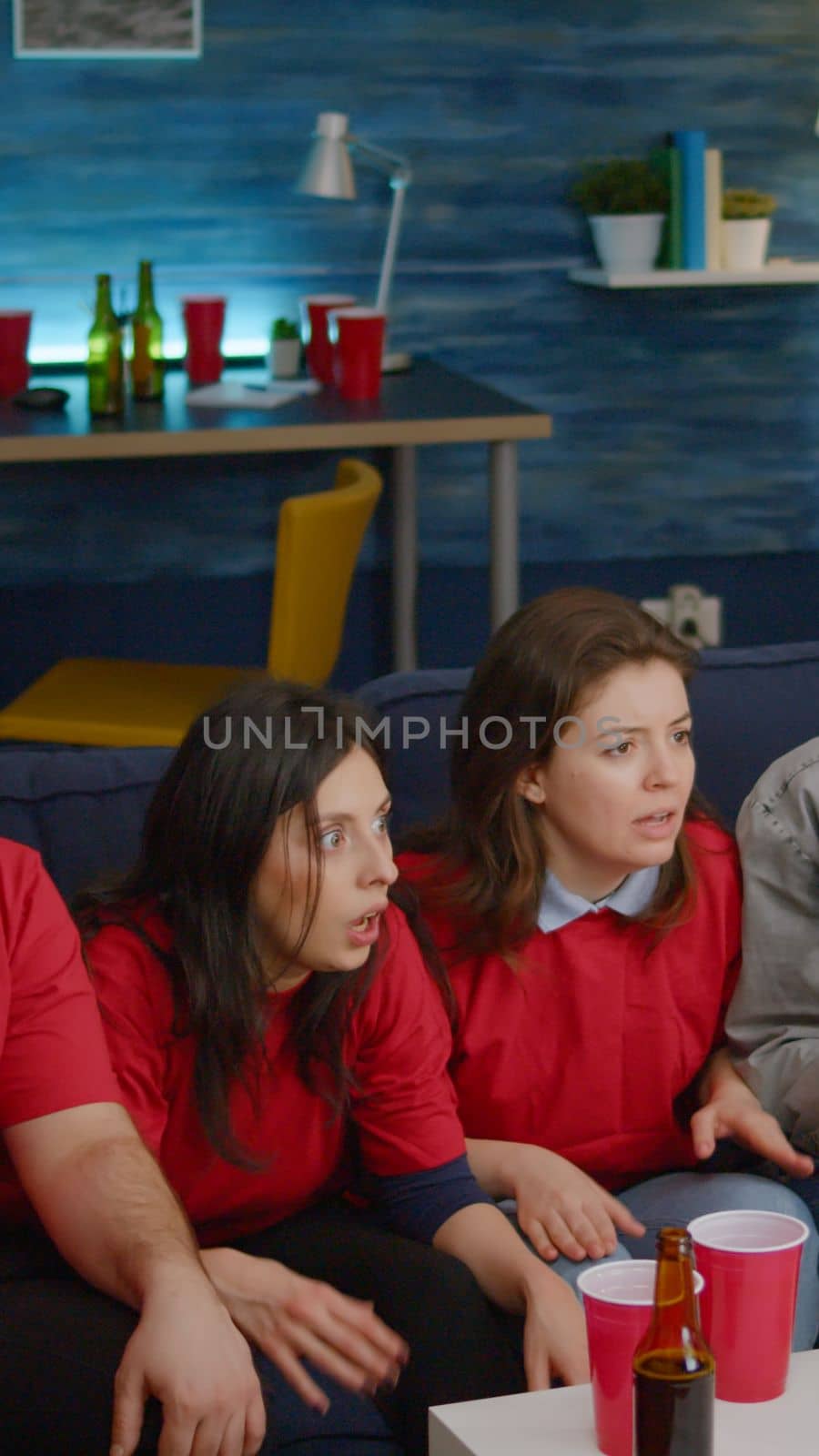 Multi ethnic friends sitting in front of television on couch while watching football by DCStudio