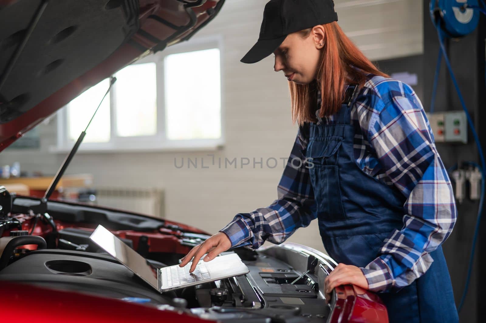 Woman auto mechanic doing engine diagnostics using laptop