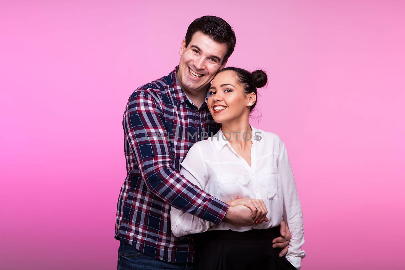 Husband embracing wife on pink background in studio photo