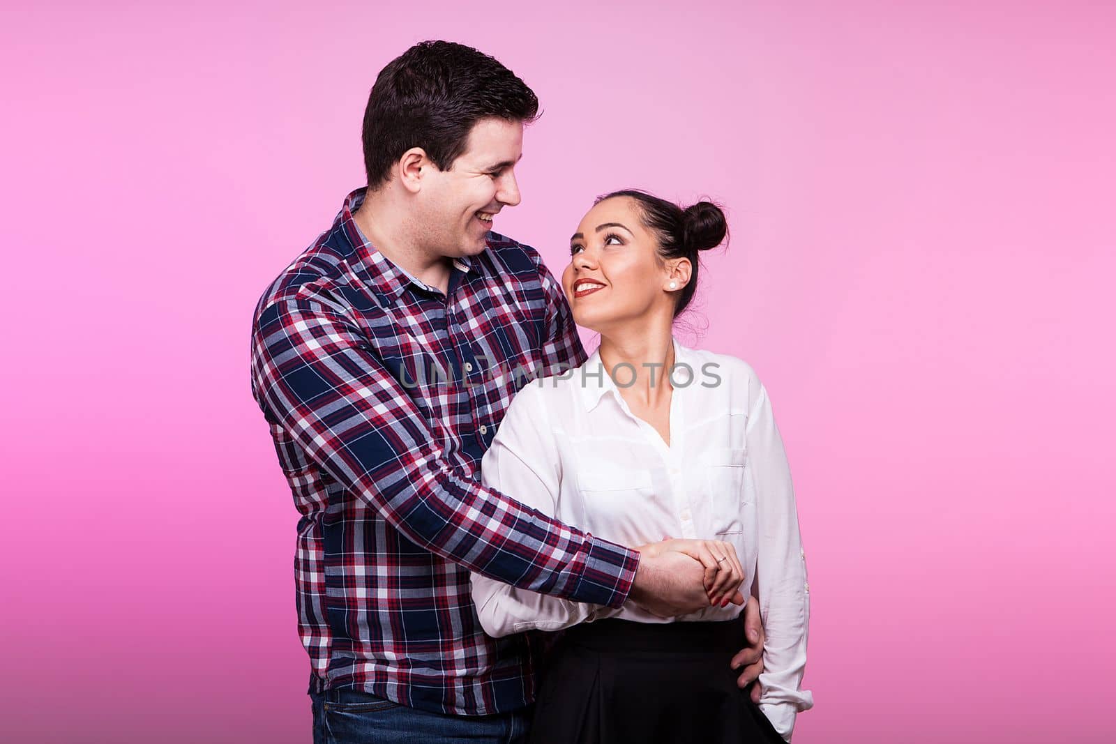 Smiling Man embracing a woman on pink background in studio photo