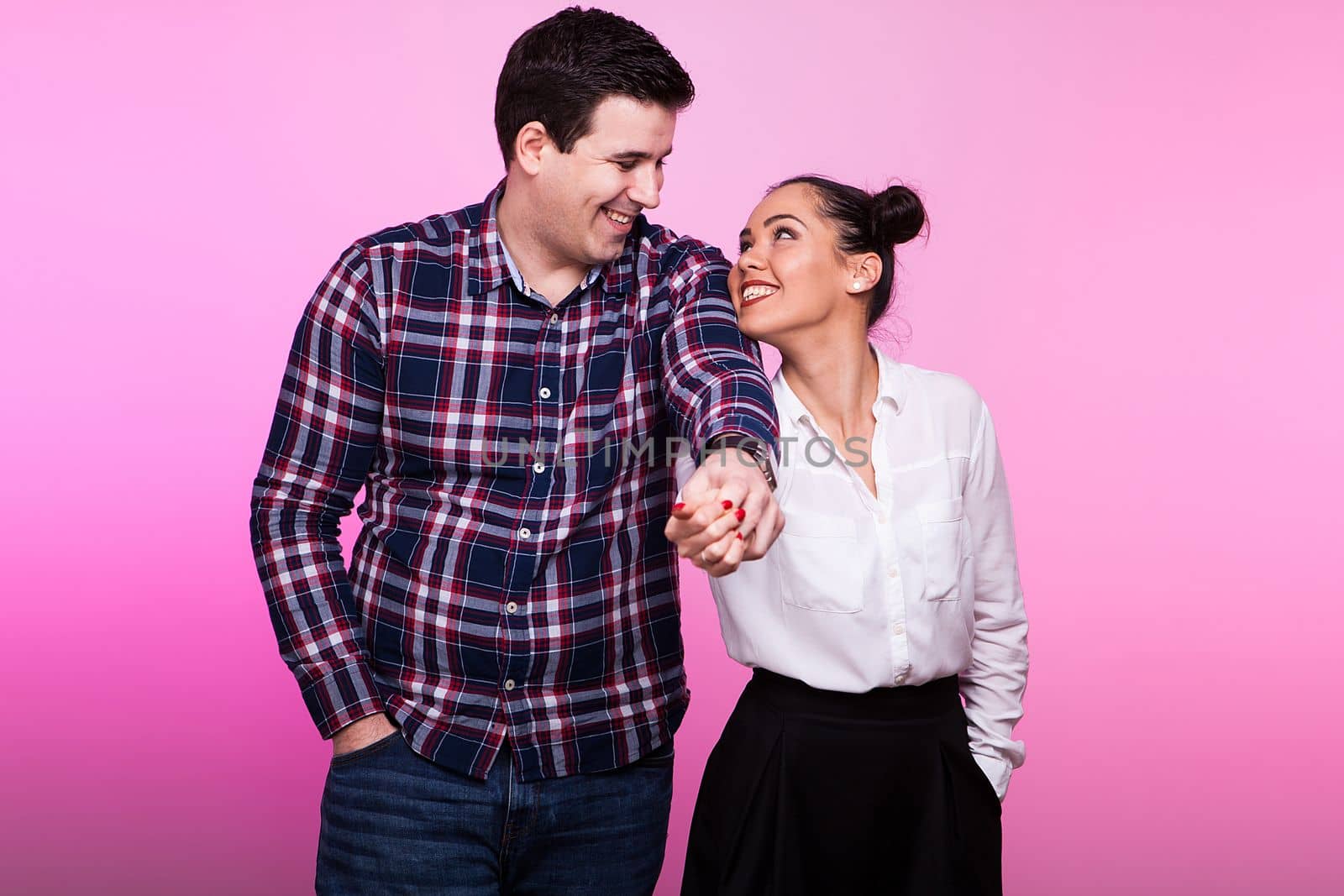 Happy inlove couple holding hands on pink background in studio