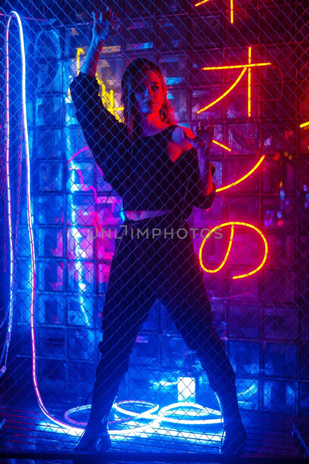 Caucasian woman in neon studio behind chain-link mesh. by mrwed54