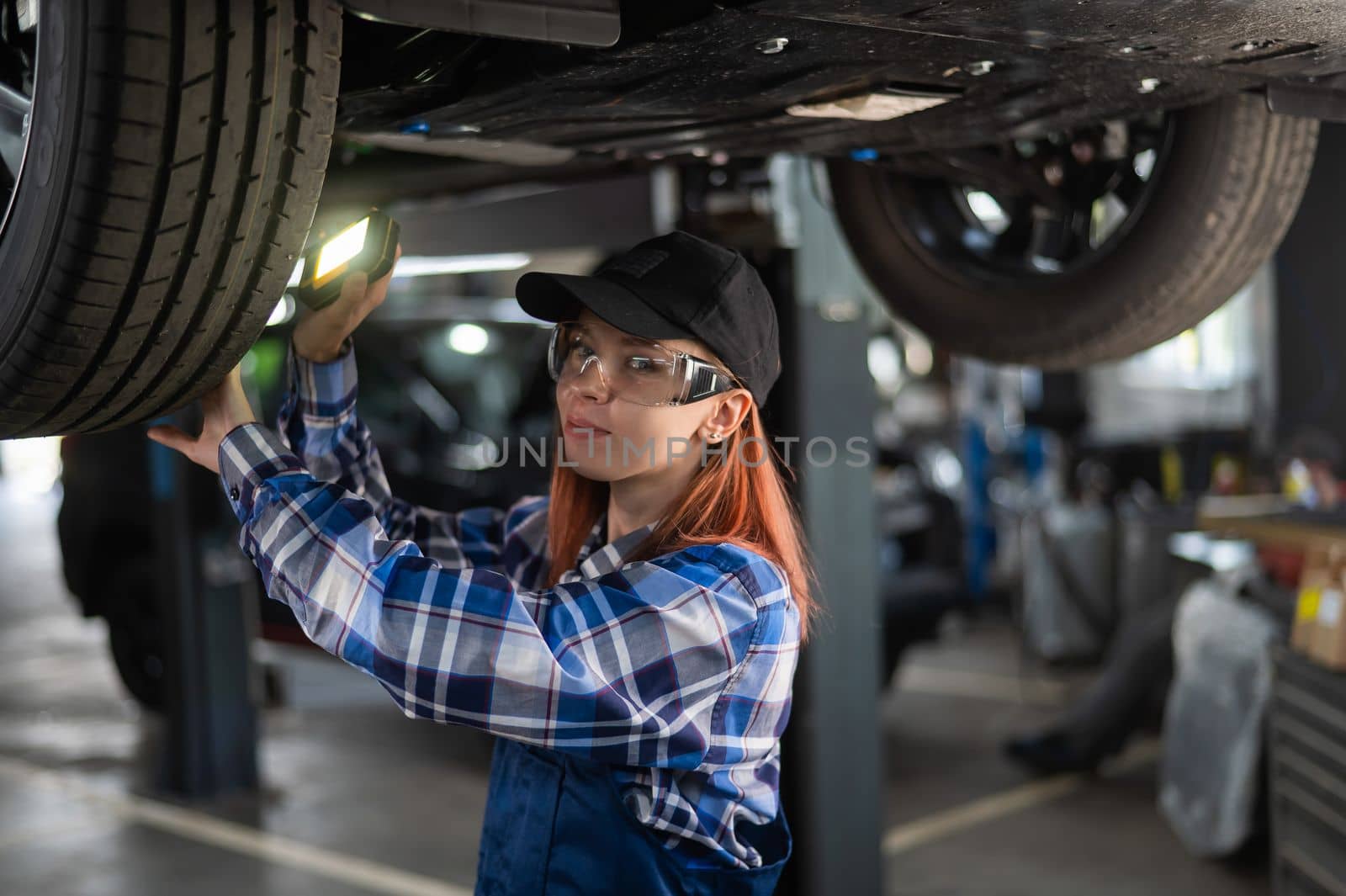 A female mechanic inspects a lifted car. A girl at a man's work