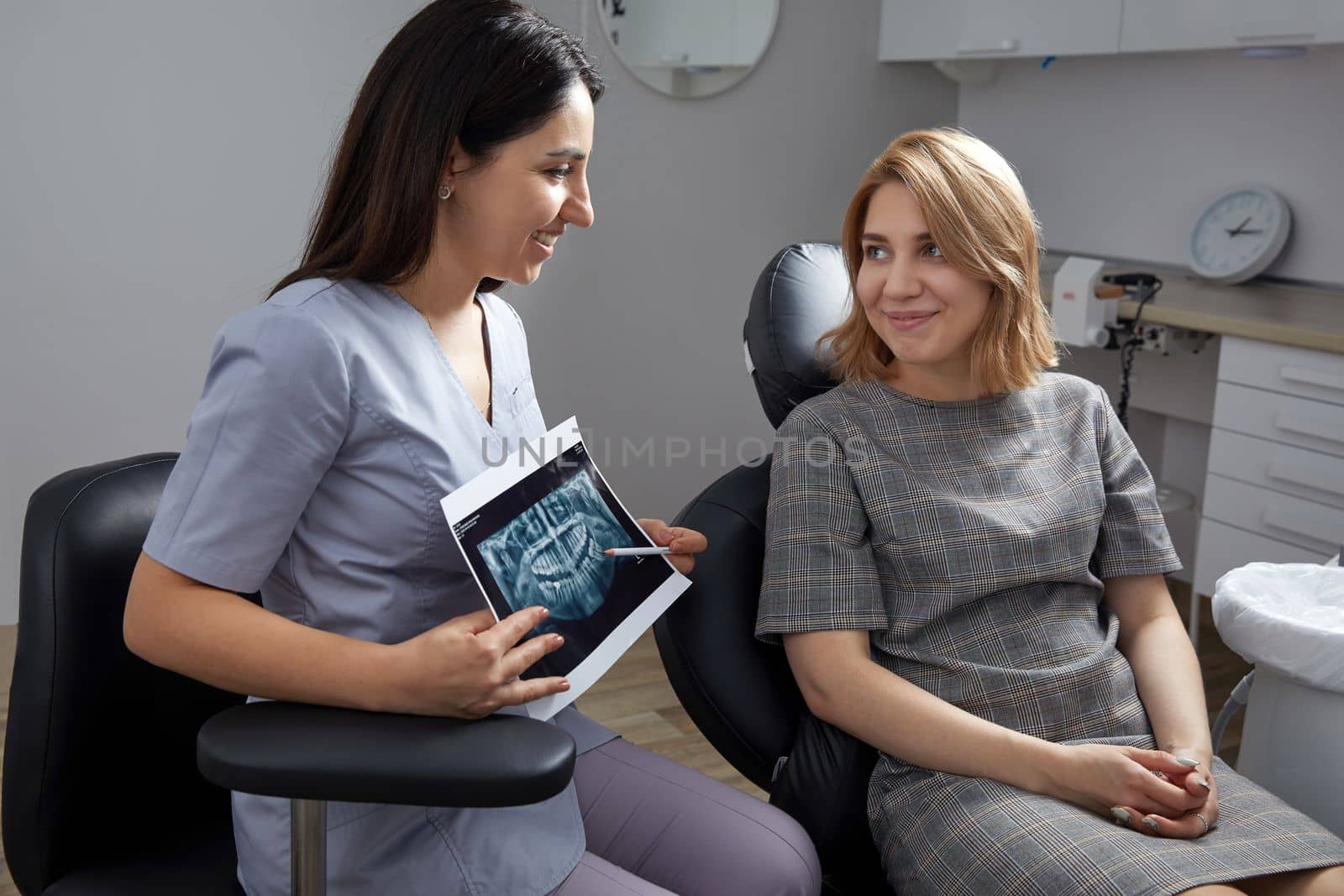 Female dentist pointing at patient's X-ray image in dental office by Mariakray