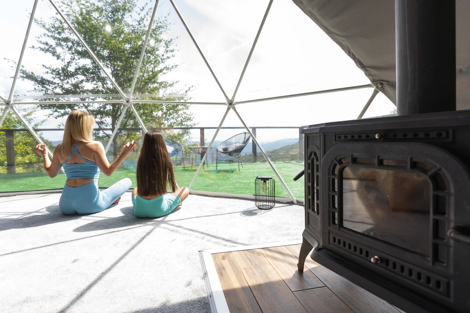mother and daughter doing yoga and meditation indoor in a glamping dome tent.
