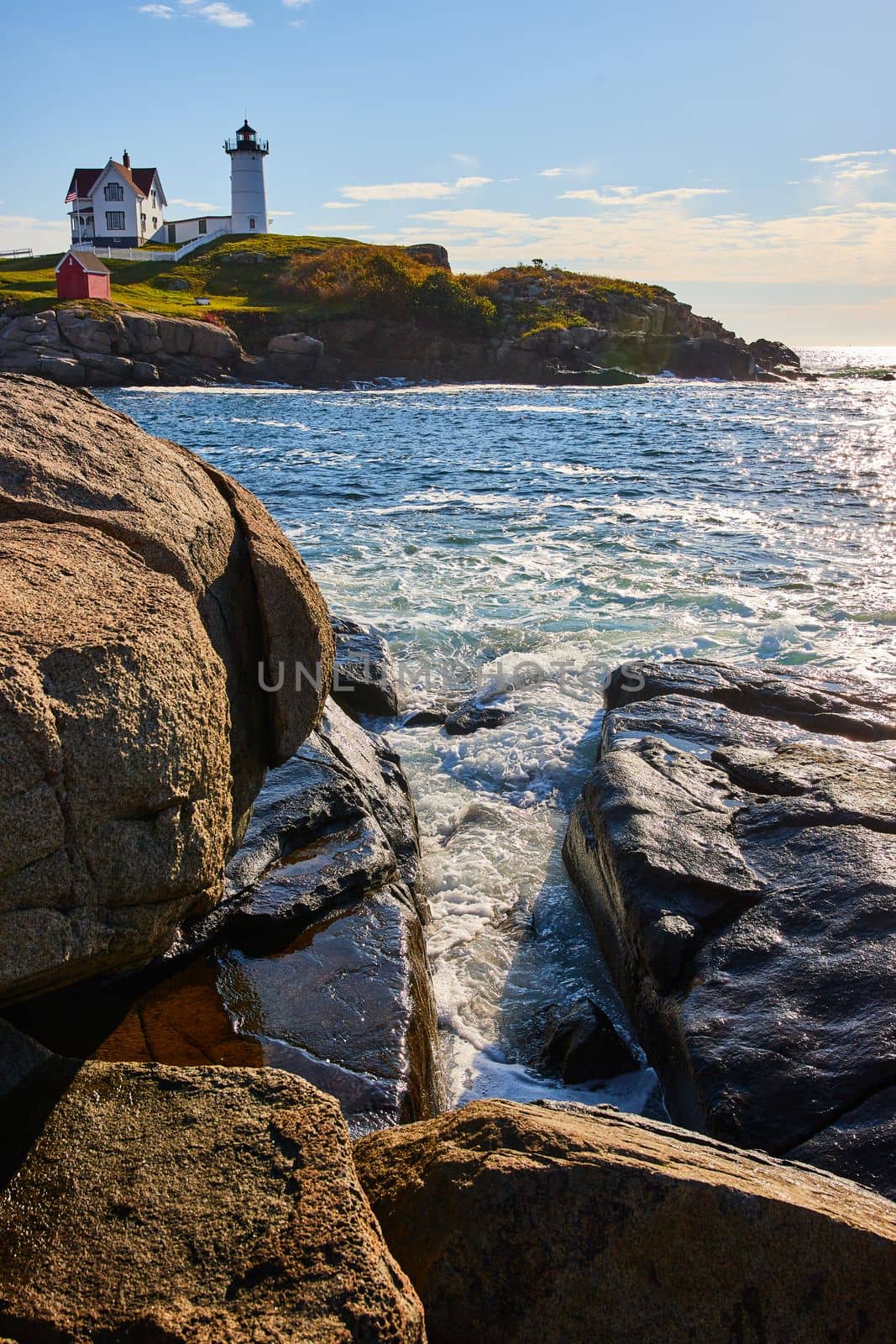 Image of Ocean waves fill crevice of rocky Maine coasts with lighthouse in background
