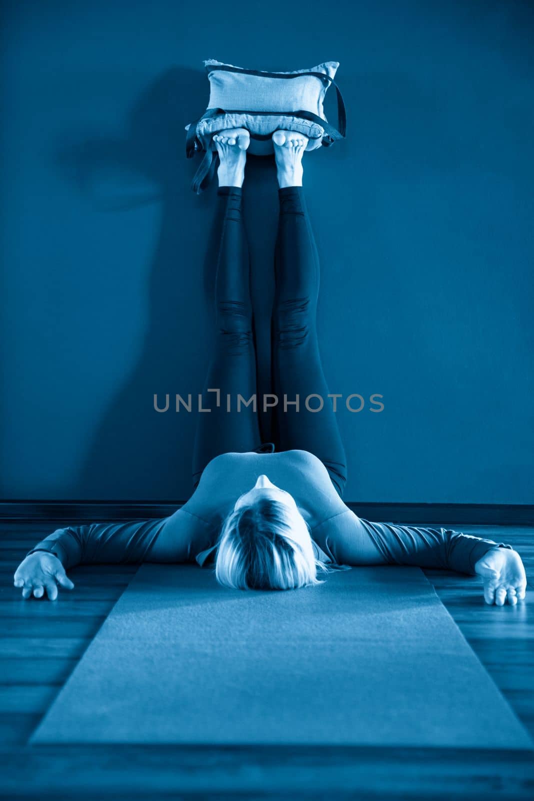 Young woman in yoga relaxing pose with legs up against wall with heavy sand bags by Mariakray