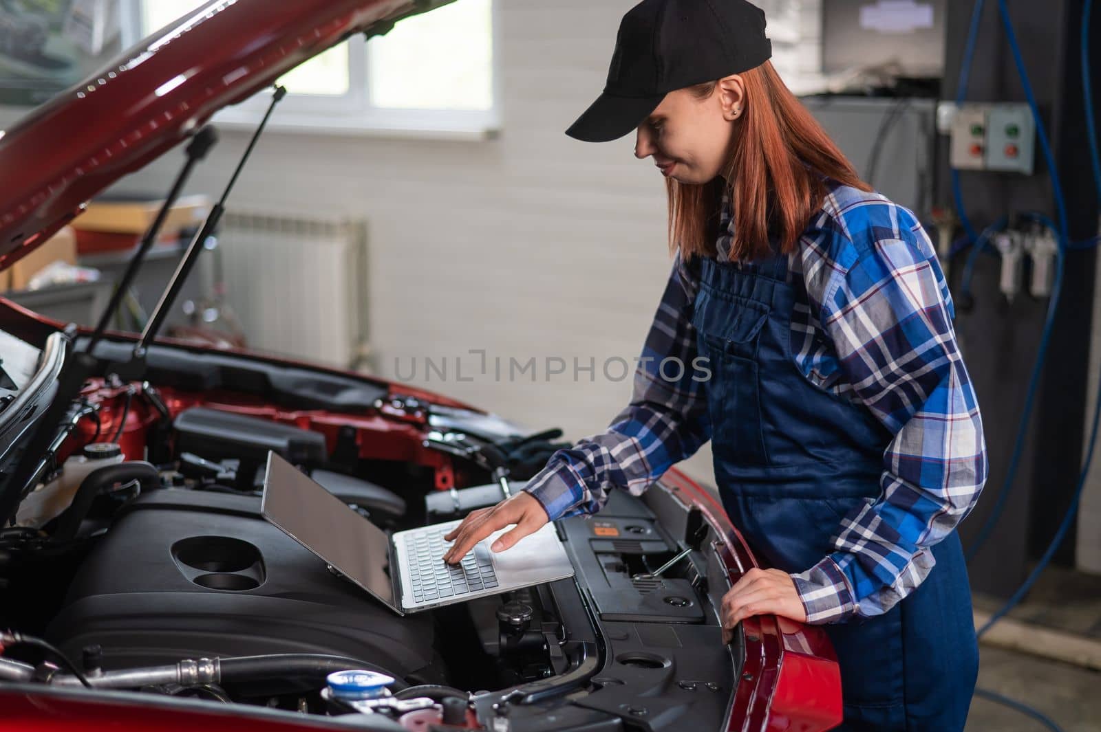 Woman auto mechanic doing engine diagnostics using laptop