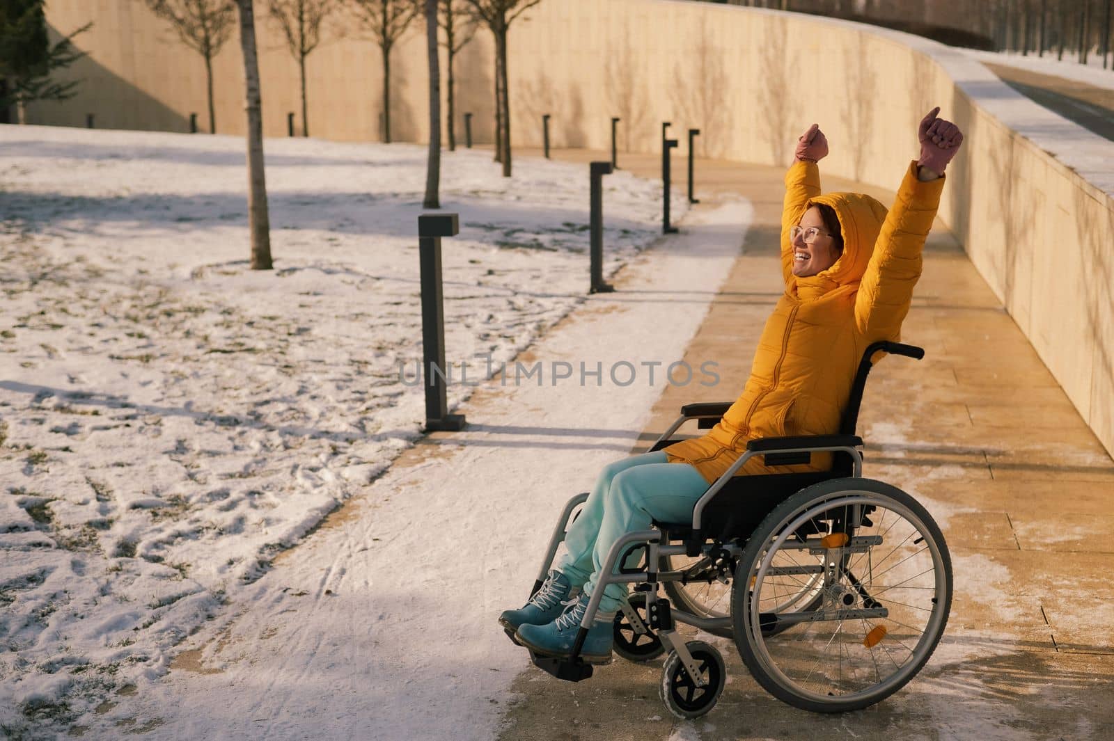 Happy woman in wheelchair happily pulls her hands up while walking in winter park