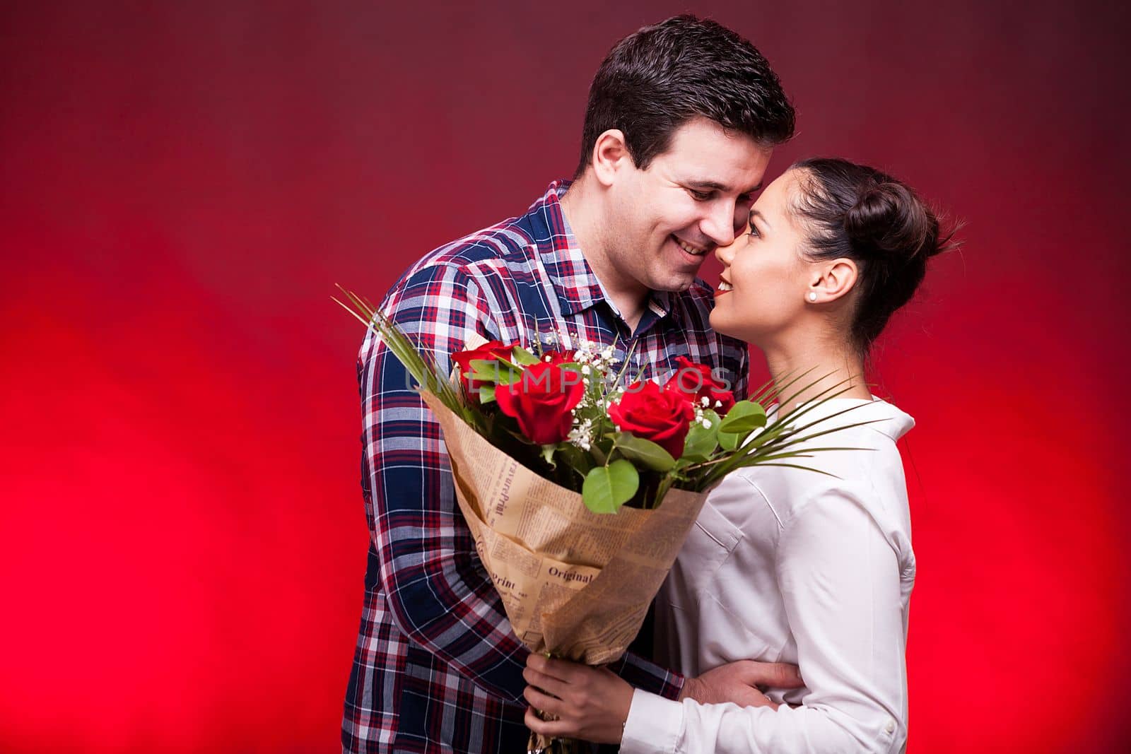 Happy couple on the first date. Woman holds a roses bouquet in hads. Red background and studio photo