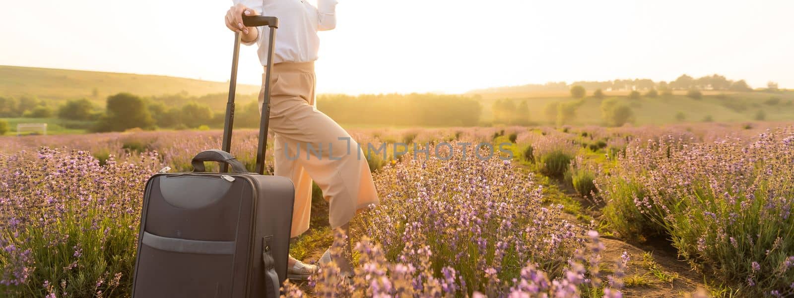 Beautiful young woman in lavender field standing with suitcase.