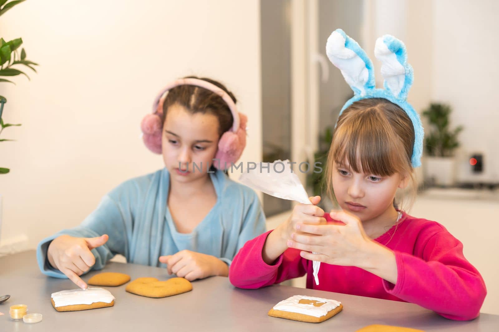 Two girls decorate cookies on plates with chocolate icing. Cooking treats for halloween celebration.