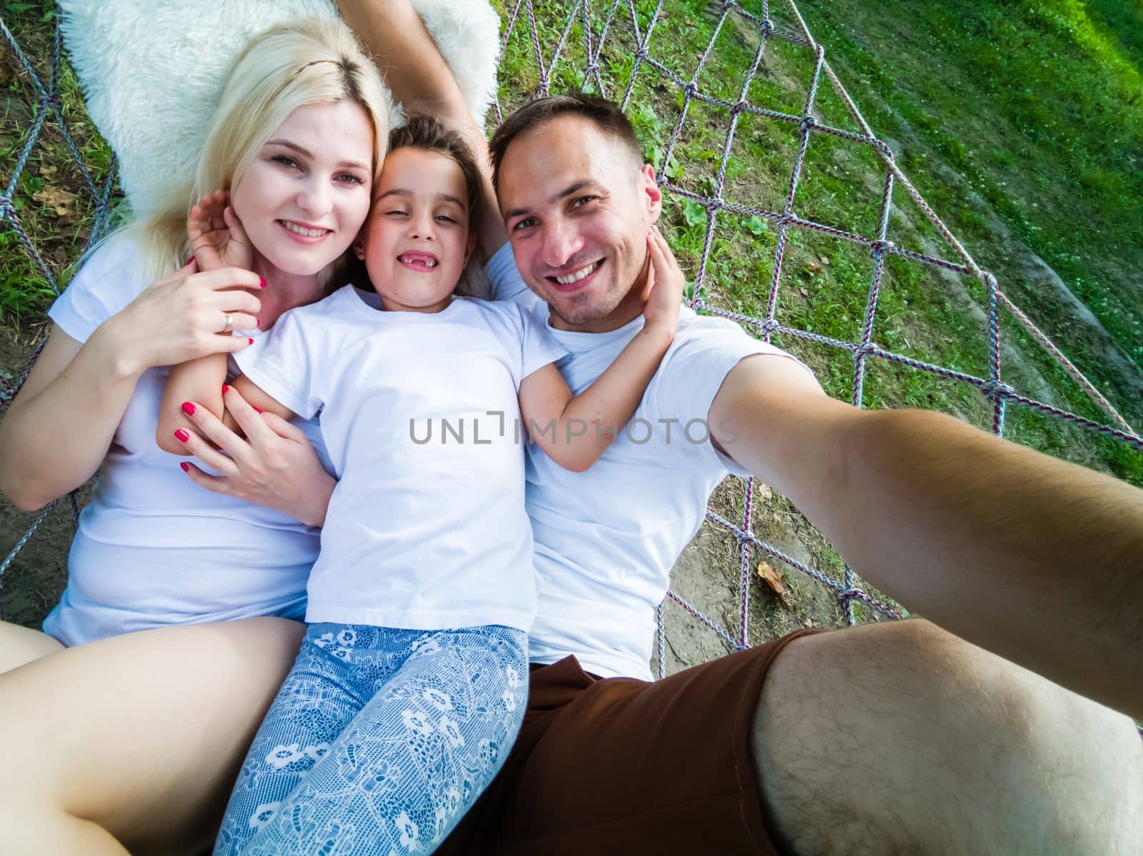 Family Relaxing In Garden Hammock Together.