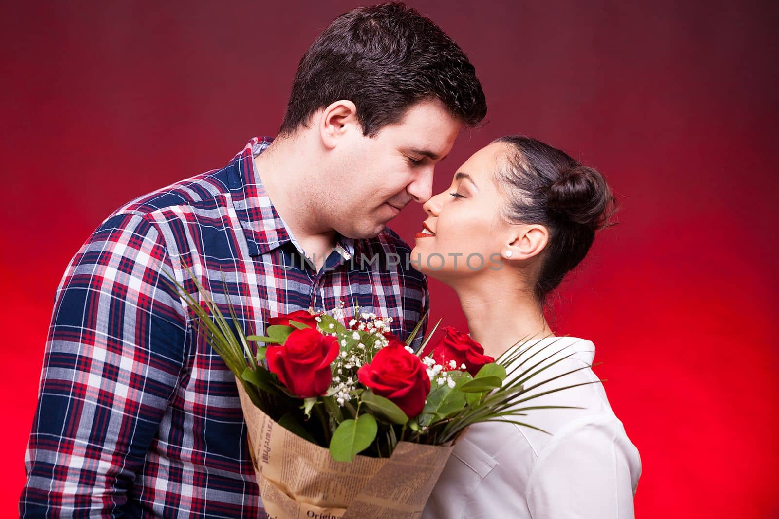 Beautiful couple with a roses bouquet in hands on red background