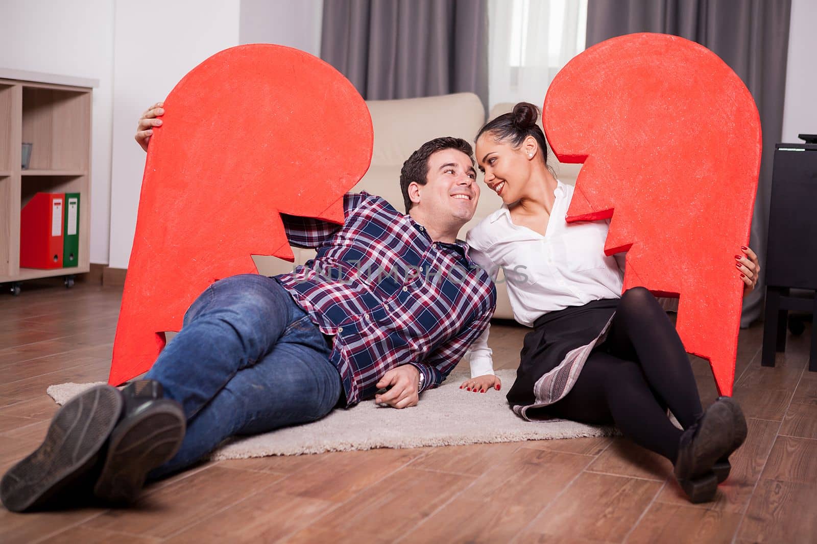 Happy couple holding two parts of one big heart lying on the floor