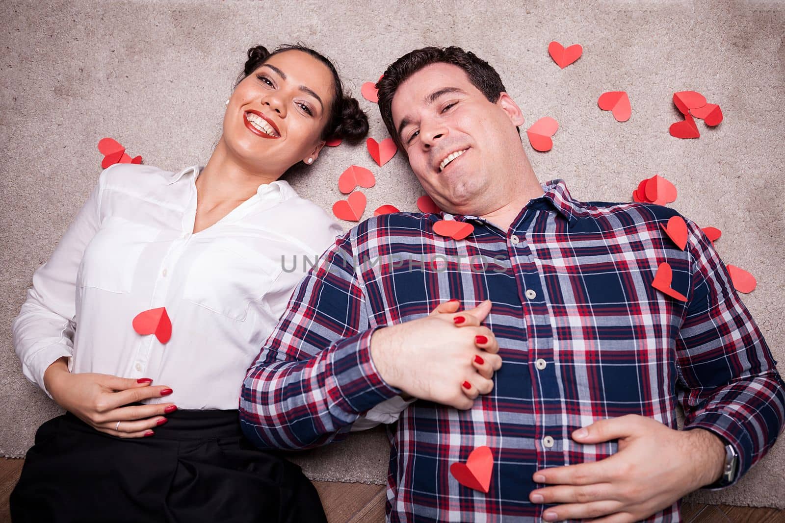 Amazing inlove couple looking at camera while lying on the floor next to small red hearts