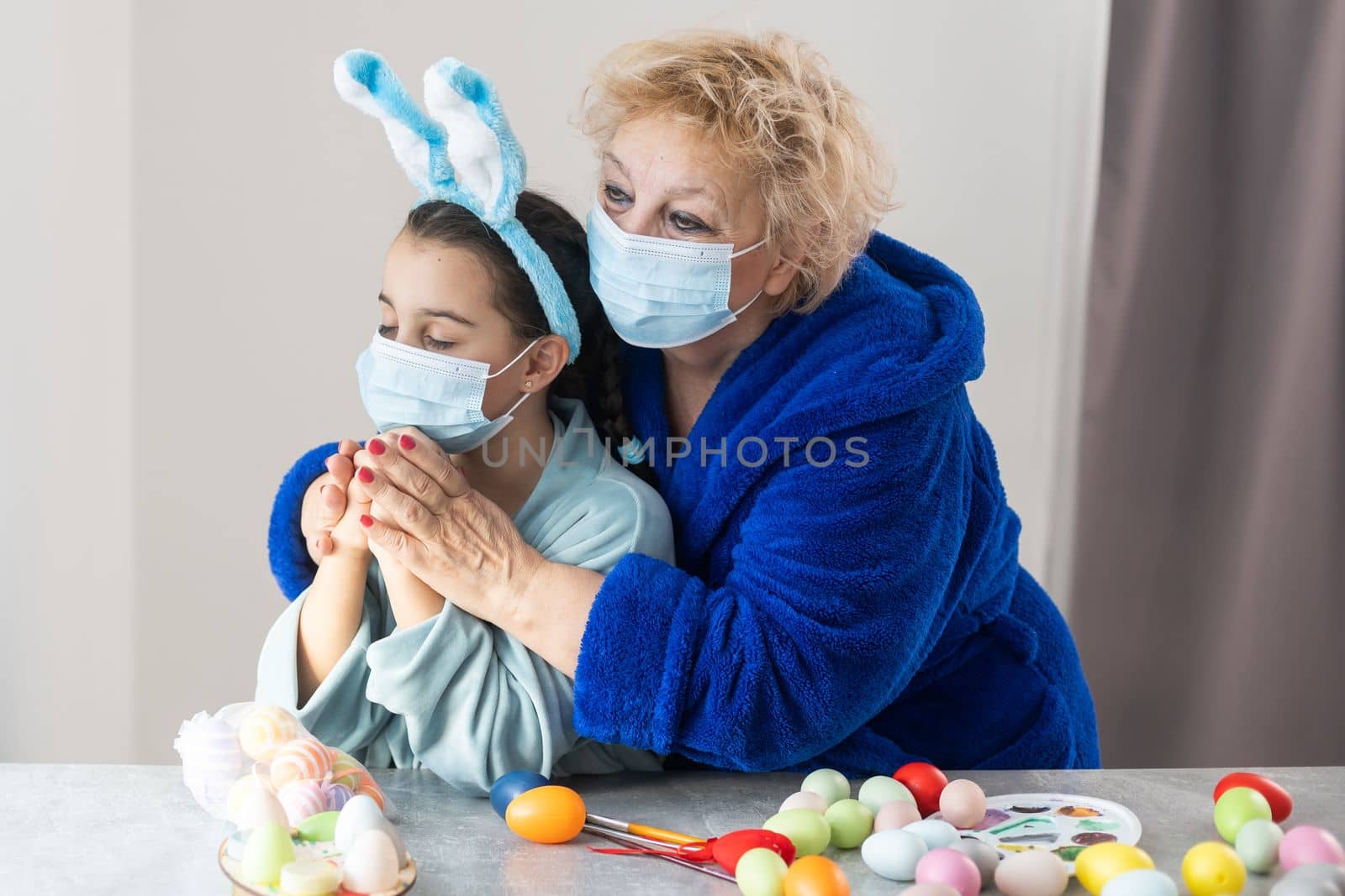 grandmother and granddaughter in medical masks are painting Easter eggs for the holiday. Happy easter family quarantined coronavirus. Happy at home. by Andelov13