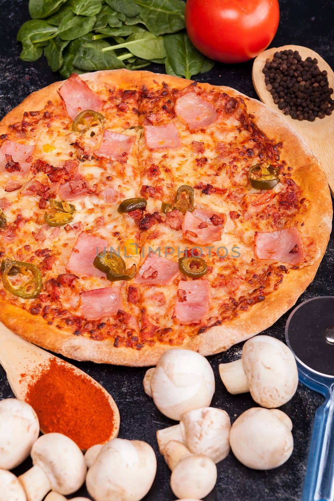 Close up of pizza surrounded with ingredients which it is made from on dark wooden table