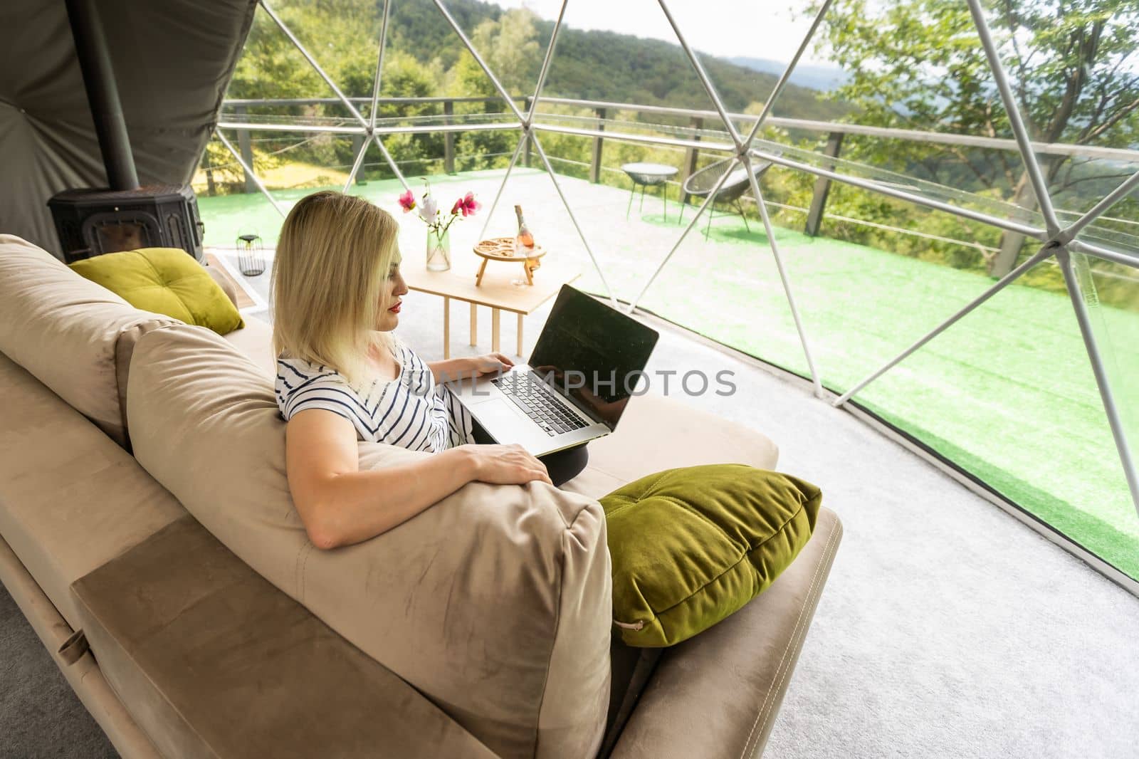 Happy young woman chatting online by using laptop in dome camping. Glamping vacation concept.