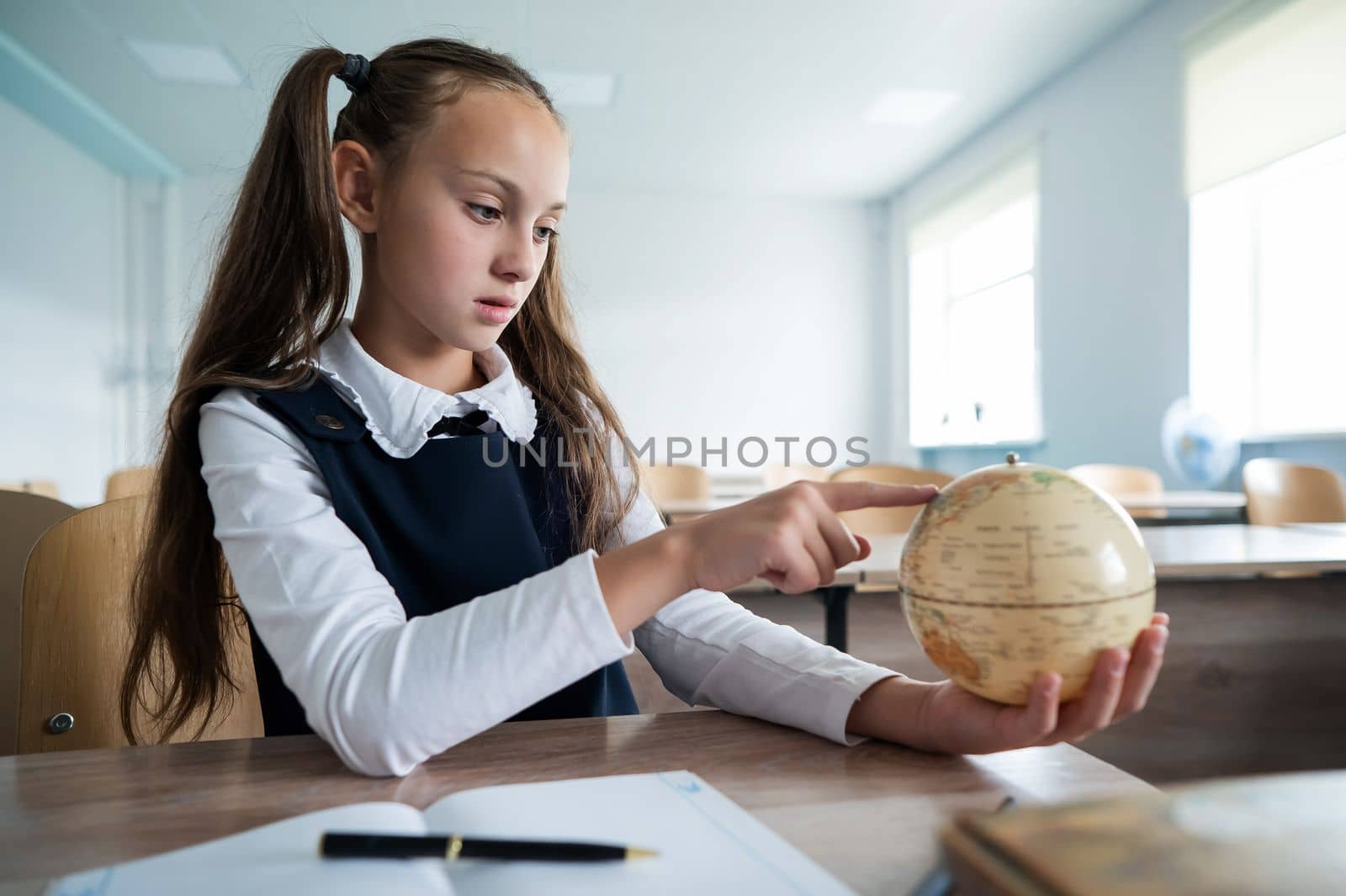 Caucasian schoolgirl sits at her desk at school and studies the globe