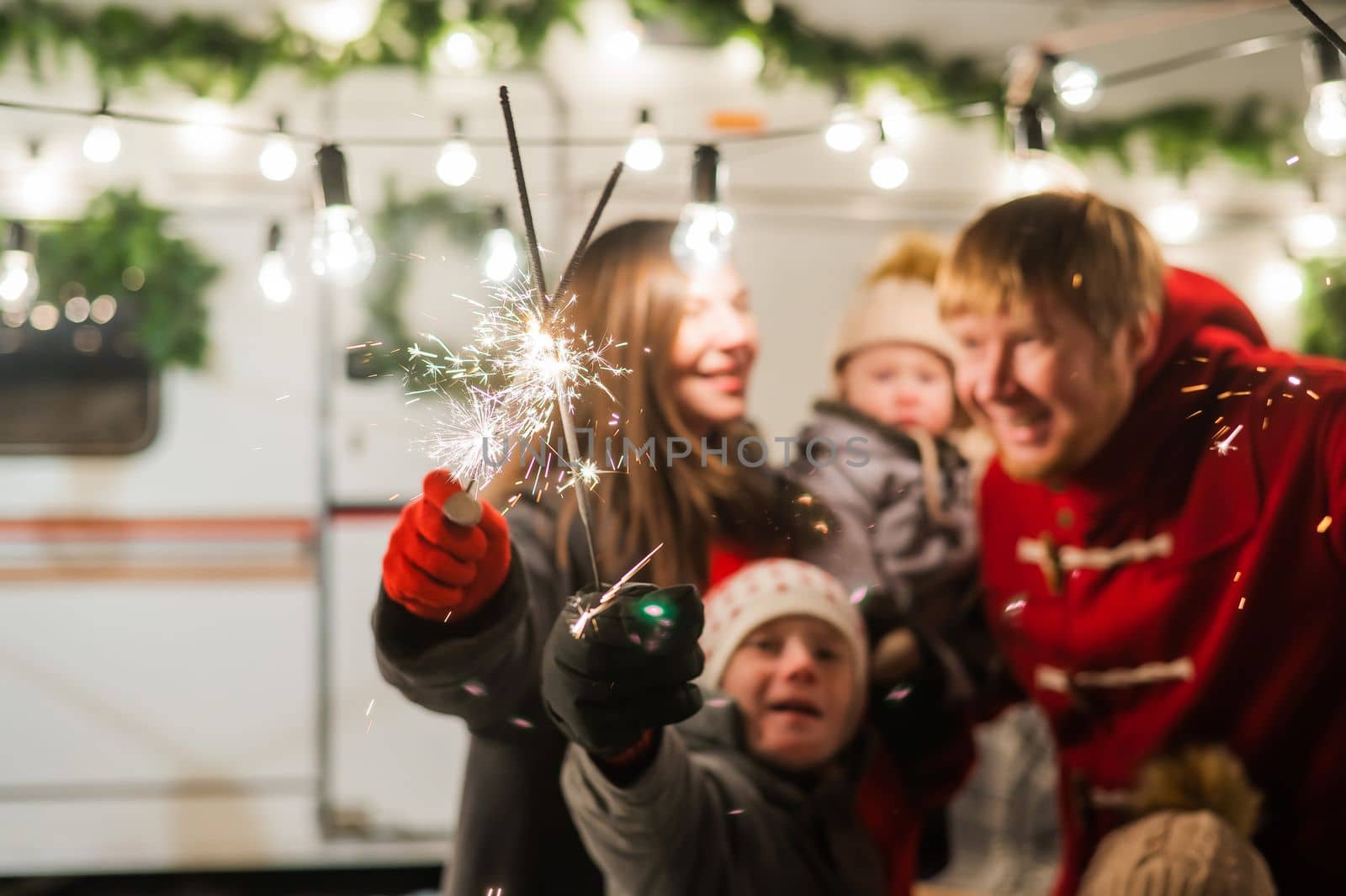 Happy large family celebrates christmas in nature and holds sparklers. Parents with three sons travels in a mobile home