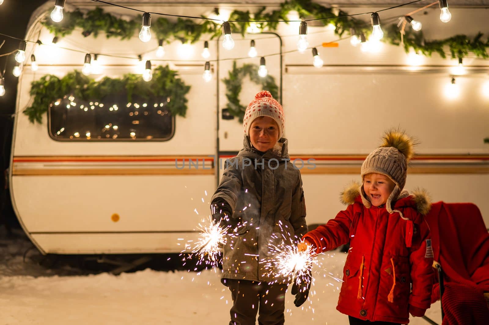 Caucasian red-haired boys hold sparklers by the trailer. Two brothers are celebrating Christmas on a trip