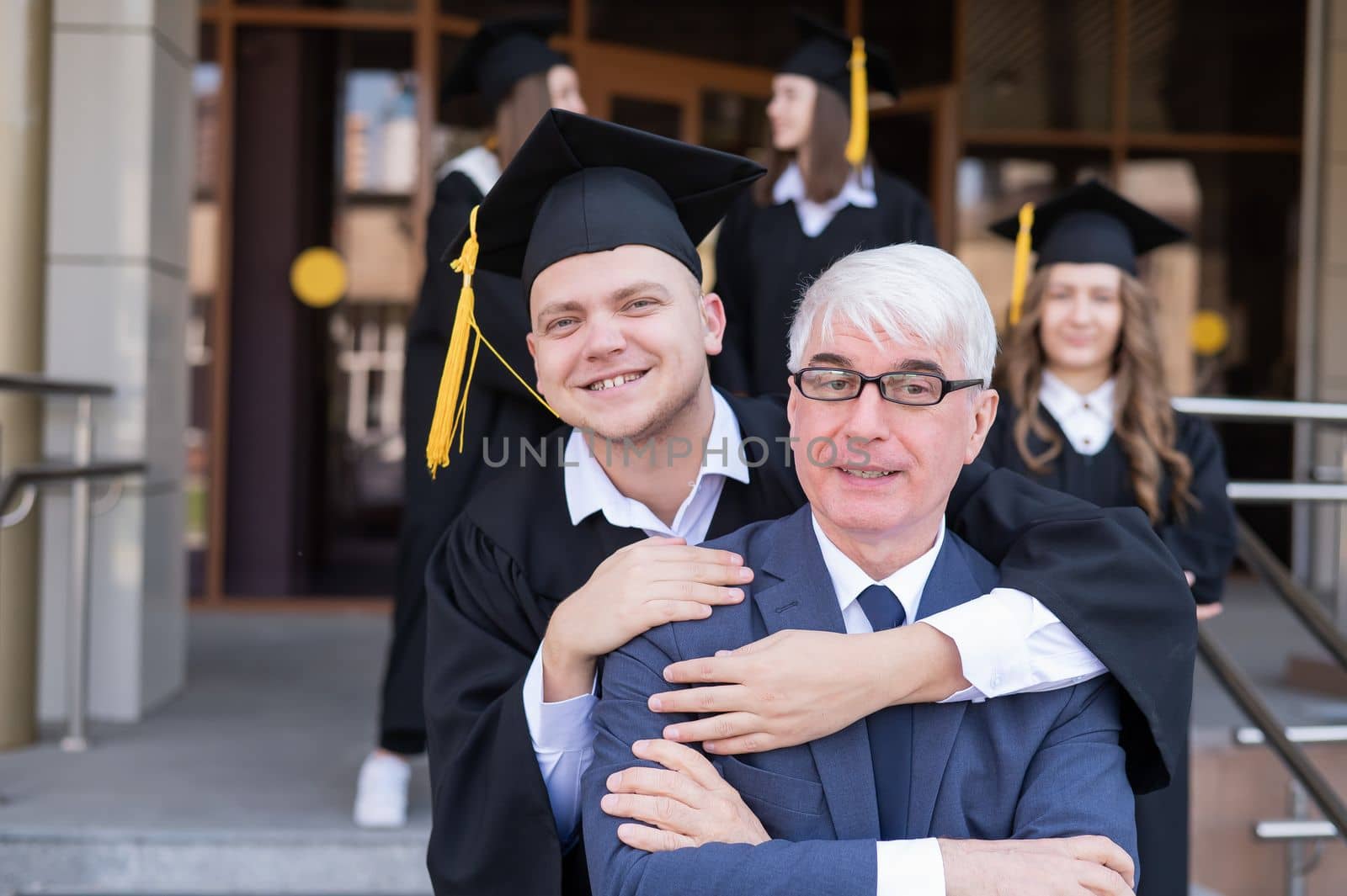 Father and son embrace at graduation. Parent congratulates university graduate. by mrwed54