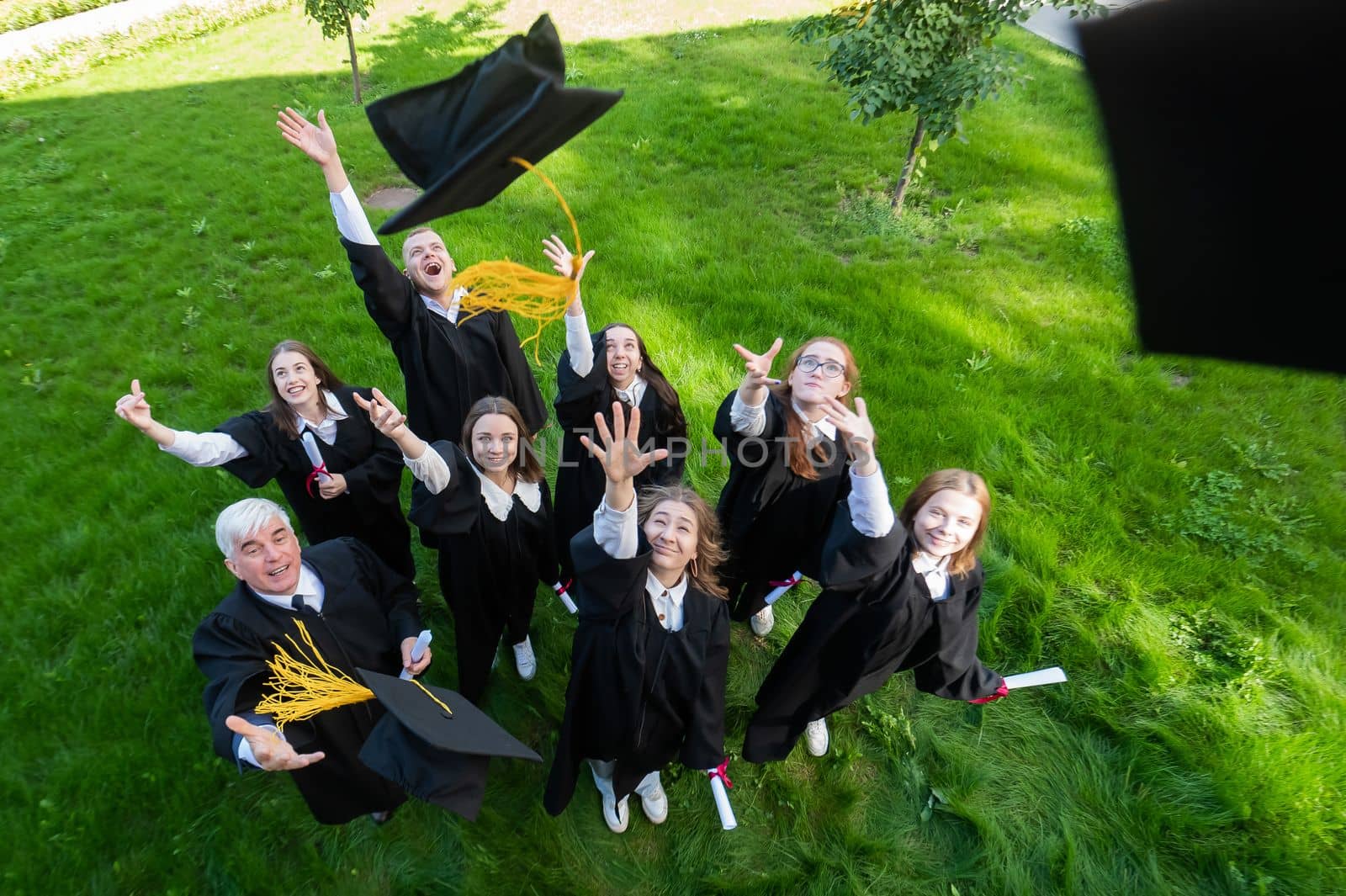 Classmates in graduation gowns throw their caps. View from above