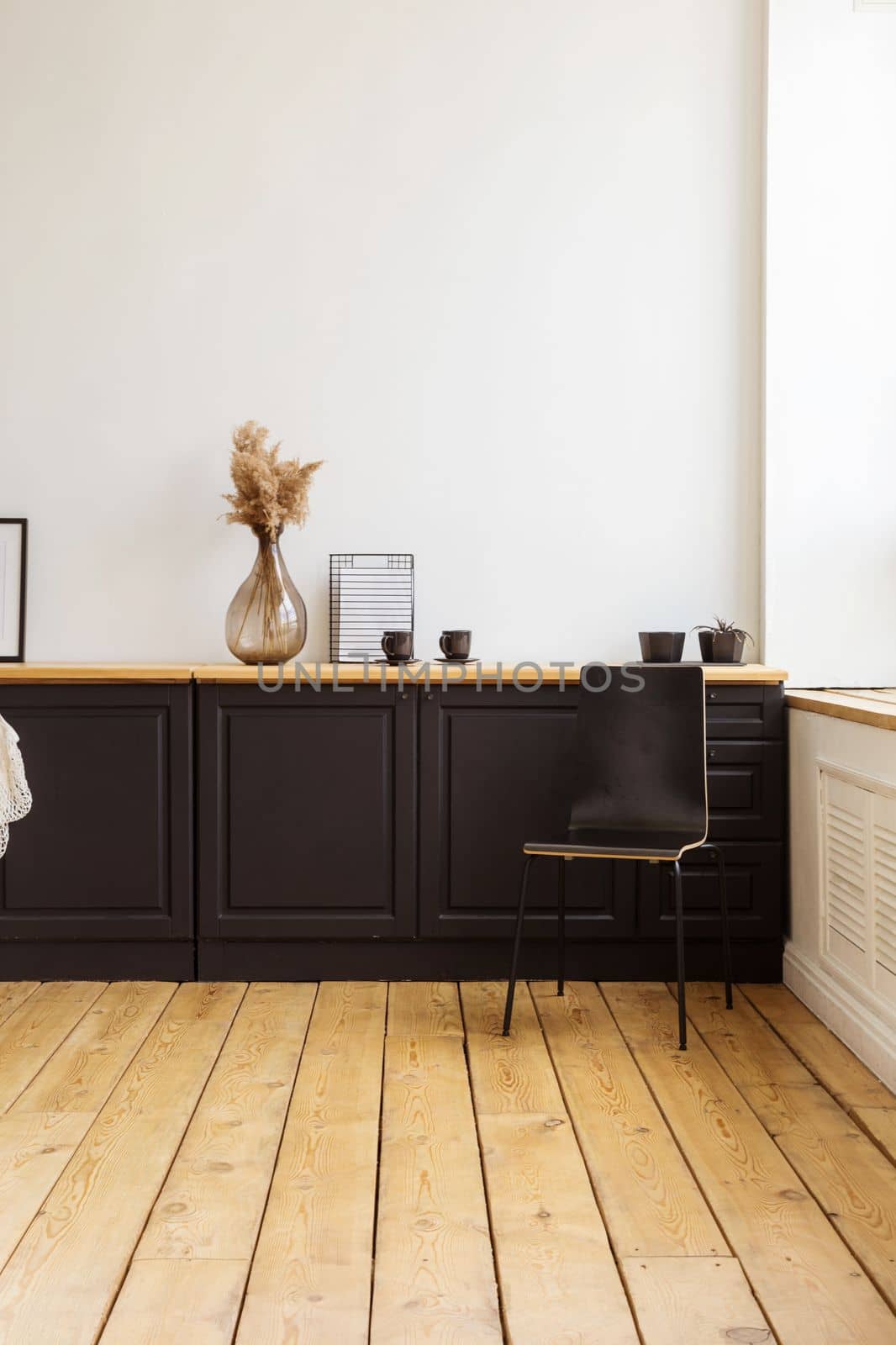 Modern cupboard with staff and various decorations placed near wooden stool against white wall in stylish apartment