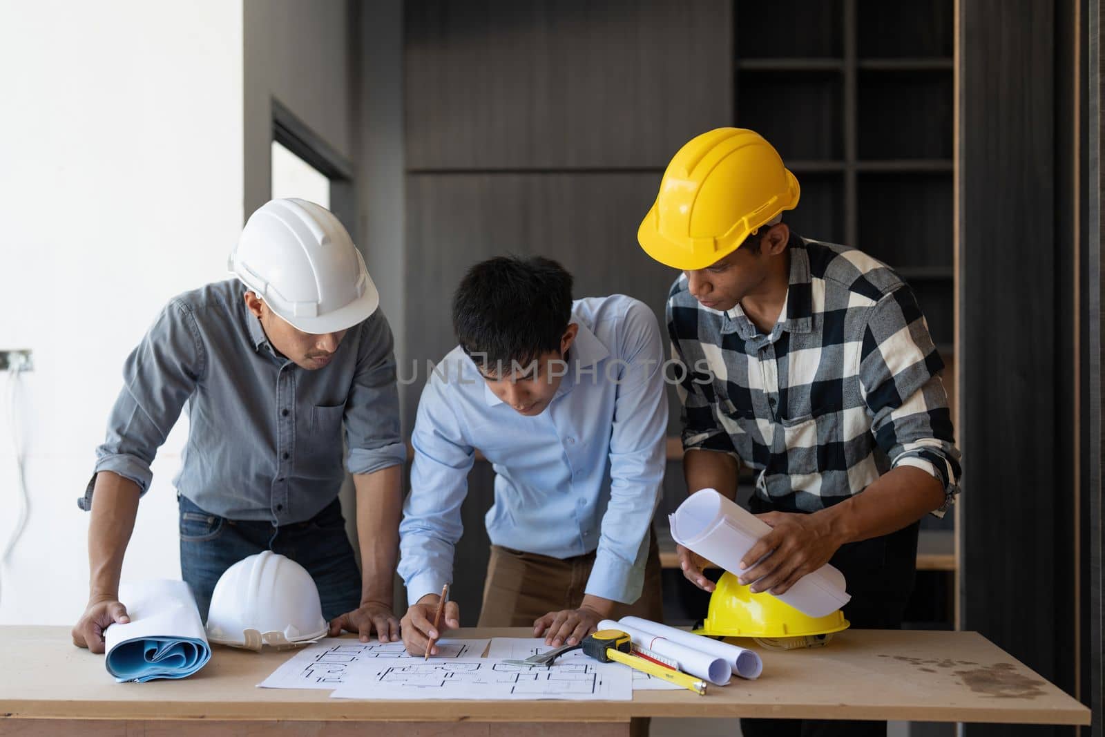 Architect team working with blueprints for architectural plan, engineer sketching a construction project, green energy concept.