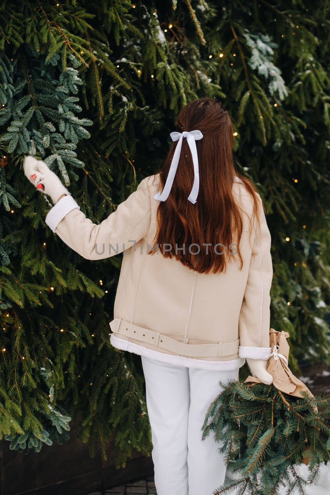 A girl with long hair stands with her back in a winter forest with a bouquet of fir branches. Snowy winter by Lobachad