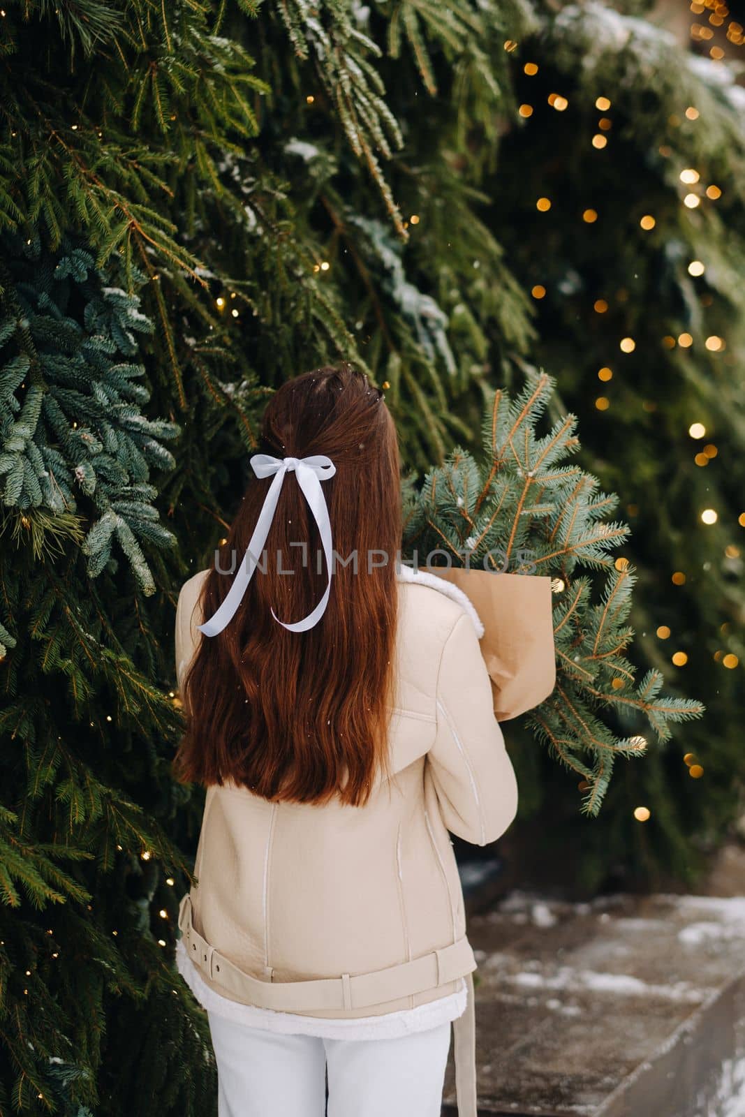 A girl with long hair stands with her back in a winter forest with a bouquet of fir branches. Snowy winter by Lobachad