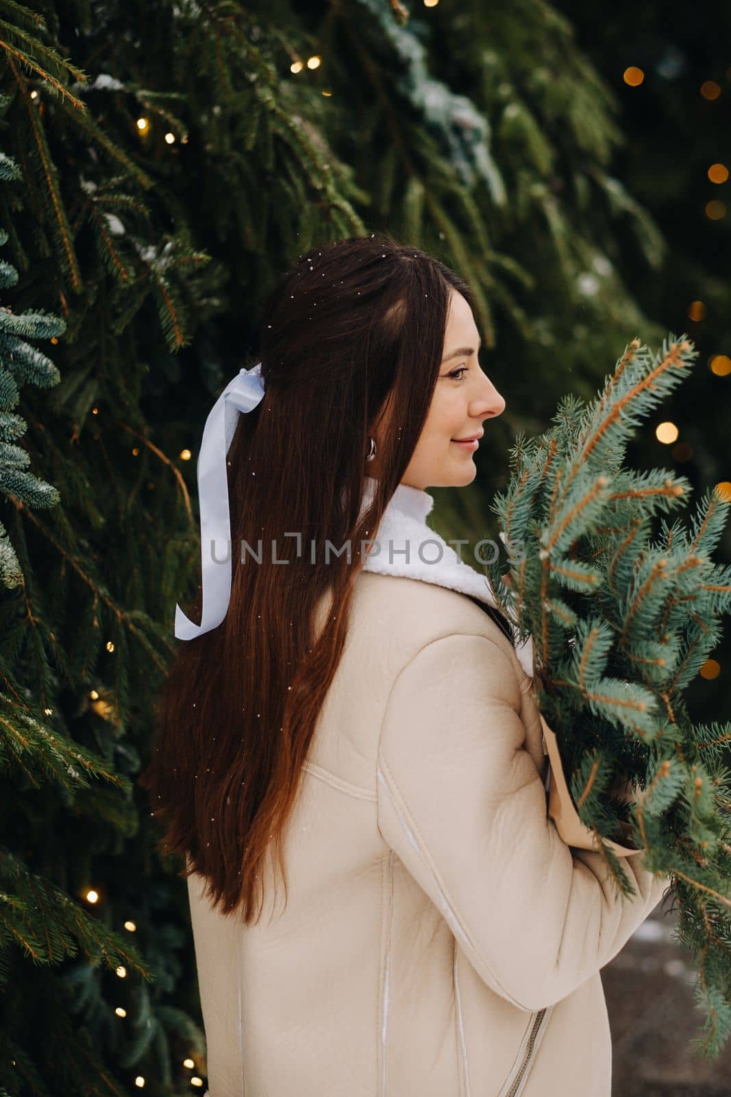 A girl with long hair stands with her back in a winter forest with a bouquet of fir branches. Snowy winter by Lobachad