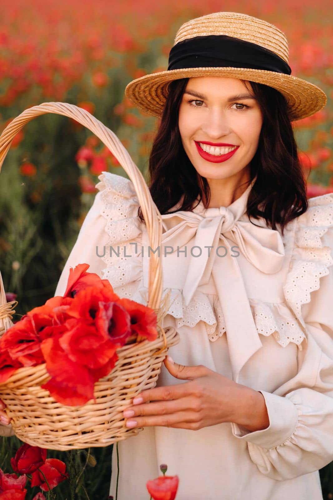 A girl in a white dress and with a basket of poppies walks through a poppy field.