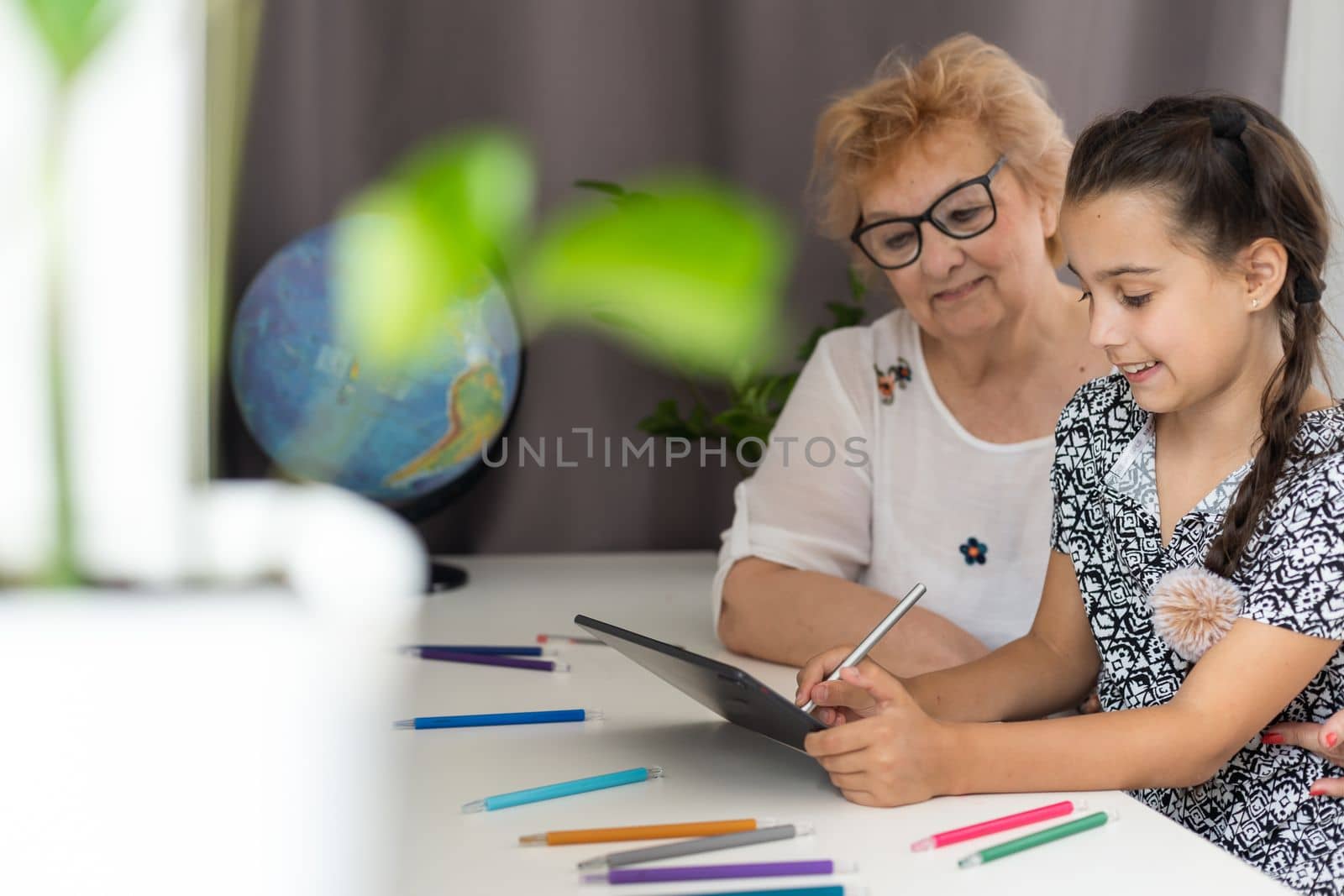 Portrait of smiling little girl teaching grandmother using digital tablet and internet in cozy home.