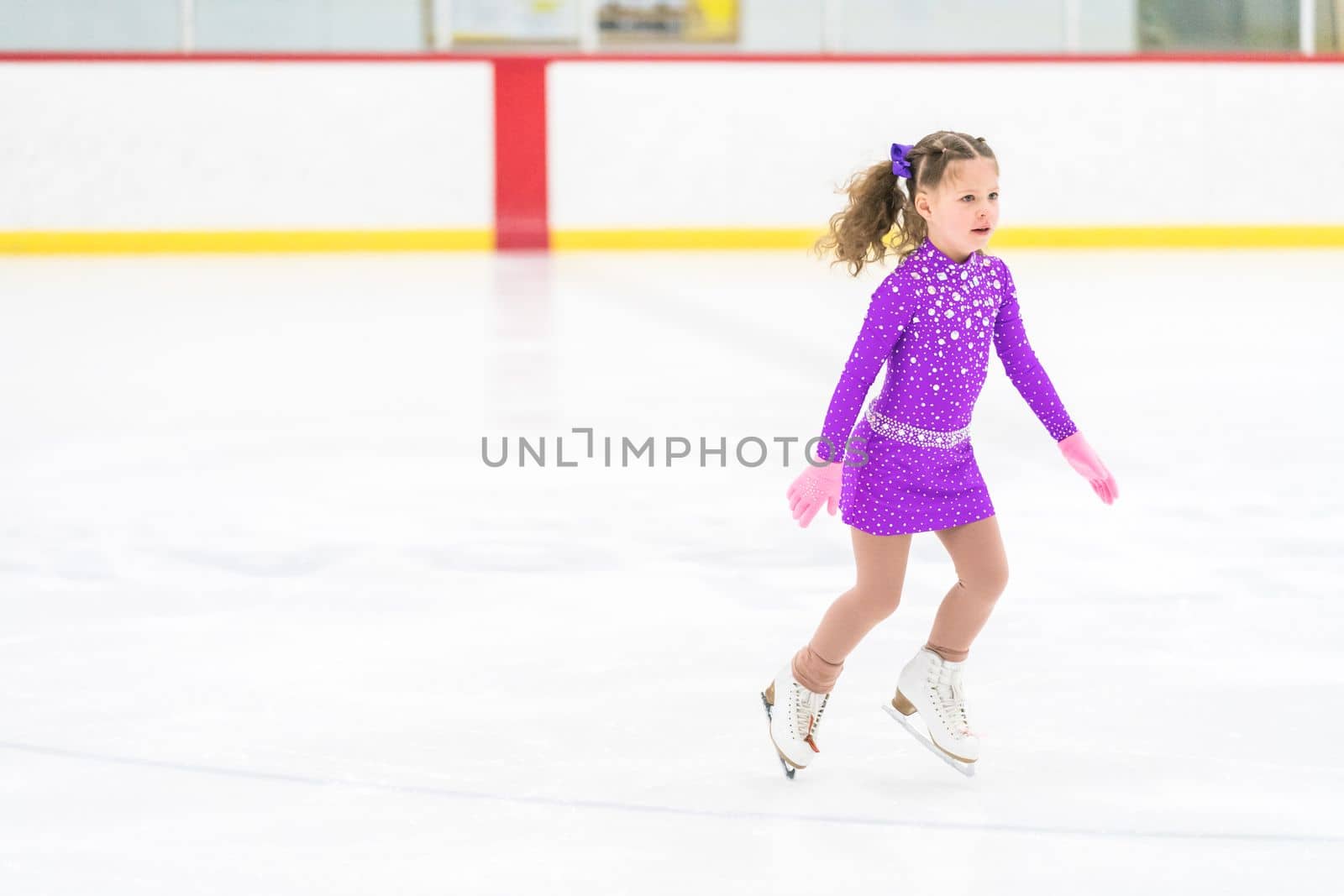 Little girl practicing figure skating on an indoor ice skating rink.