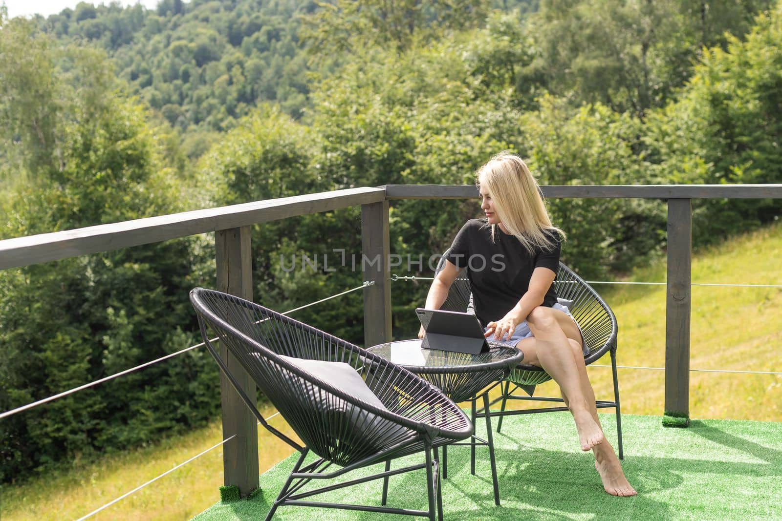 Beautiful girl works with tablet computer on a terrace in the mountains