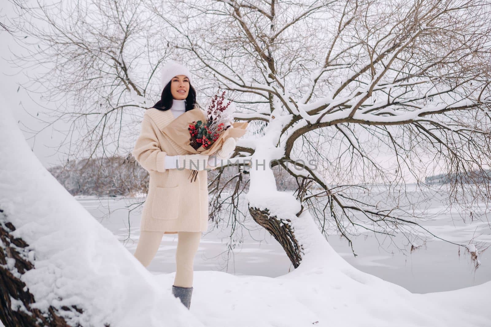 A girl in a beige cardigan and winter flowers walks in nature in the snowy season. Winter weather.