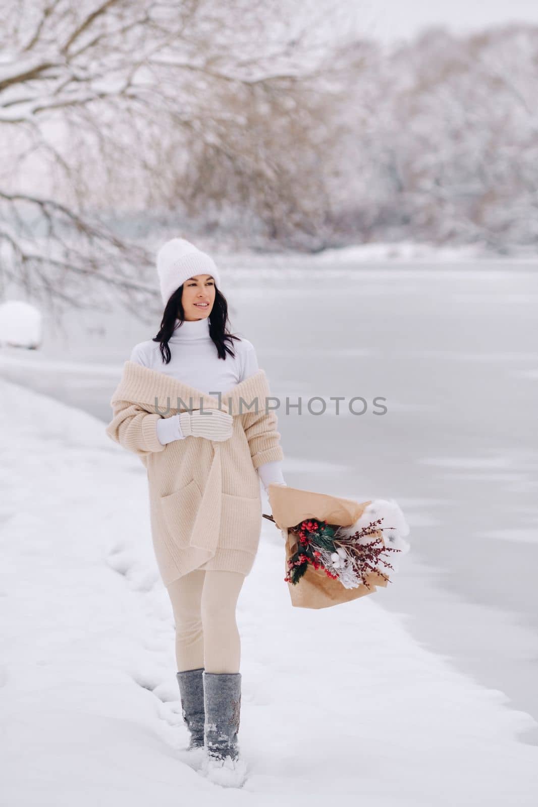 A girl in a beige cardigan and winter flowers walks in nature in the snowy season. Winter weather by Lobachad