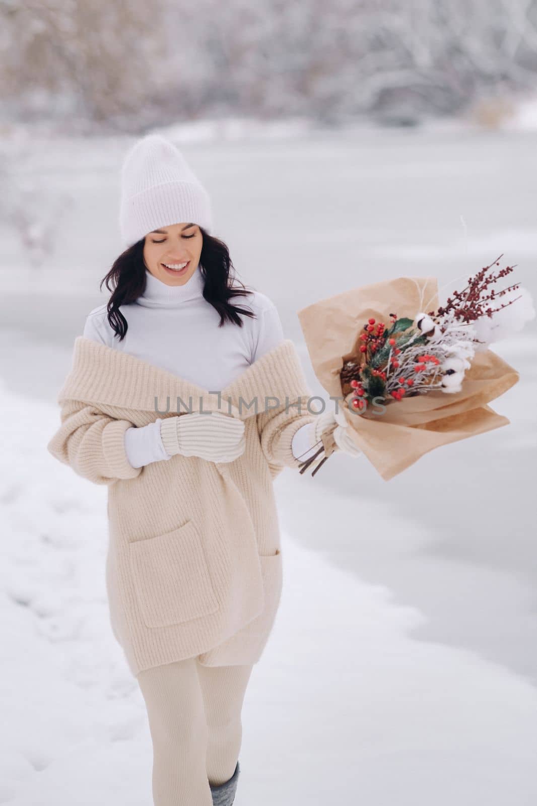 A girl in a beige cardigan and winter flowers walks in nature in the snowy season. Winter weather by Lobachad