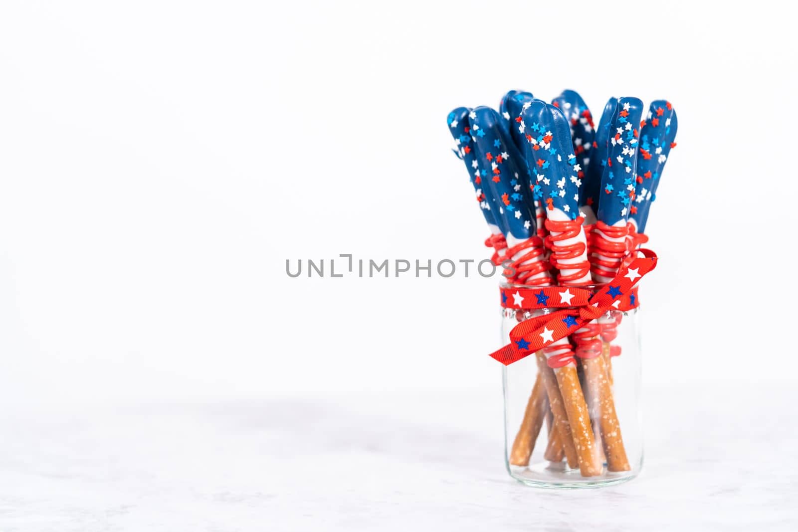 Homemade chocolate-covered pretzel rods decorated like the American flag in a glass jar.