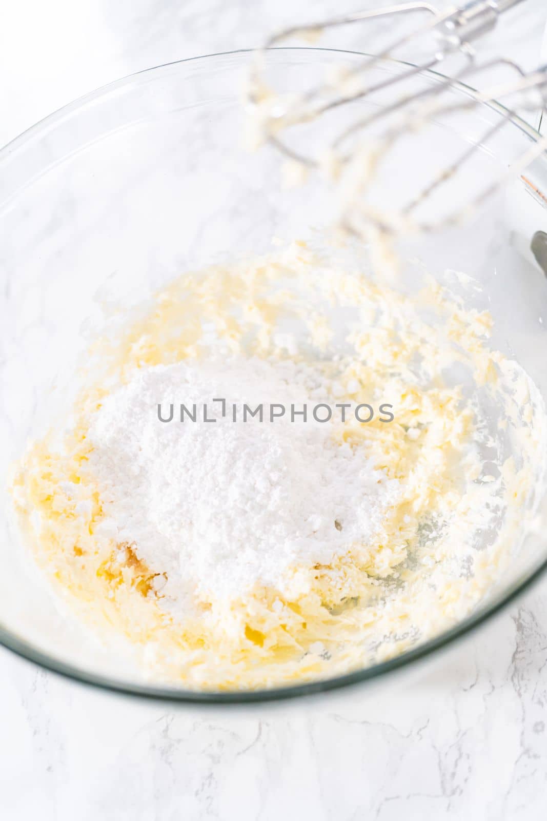 Mixing ingredients in a large glass mixing bowl to prepare cream cheese drizzle sauce.