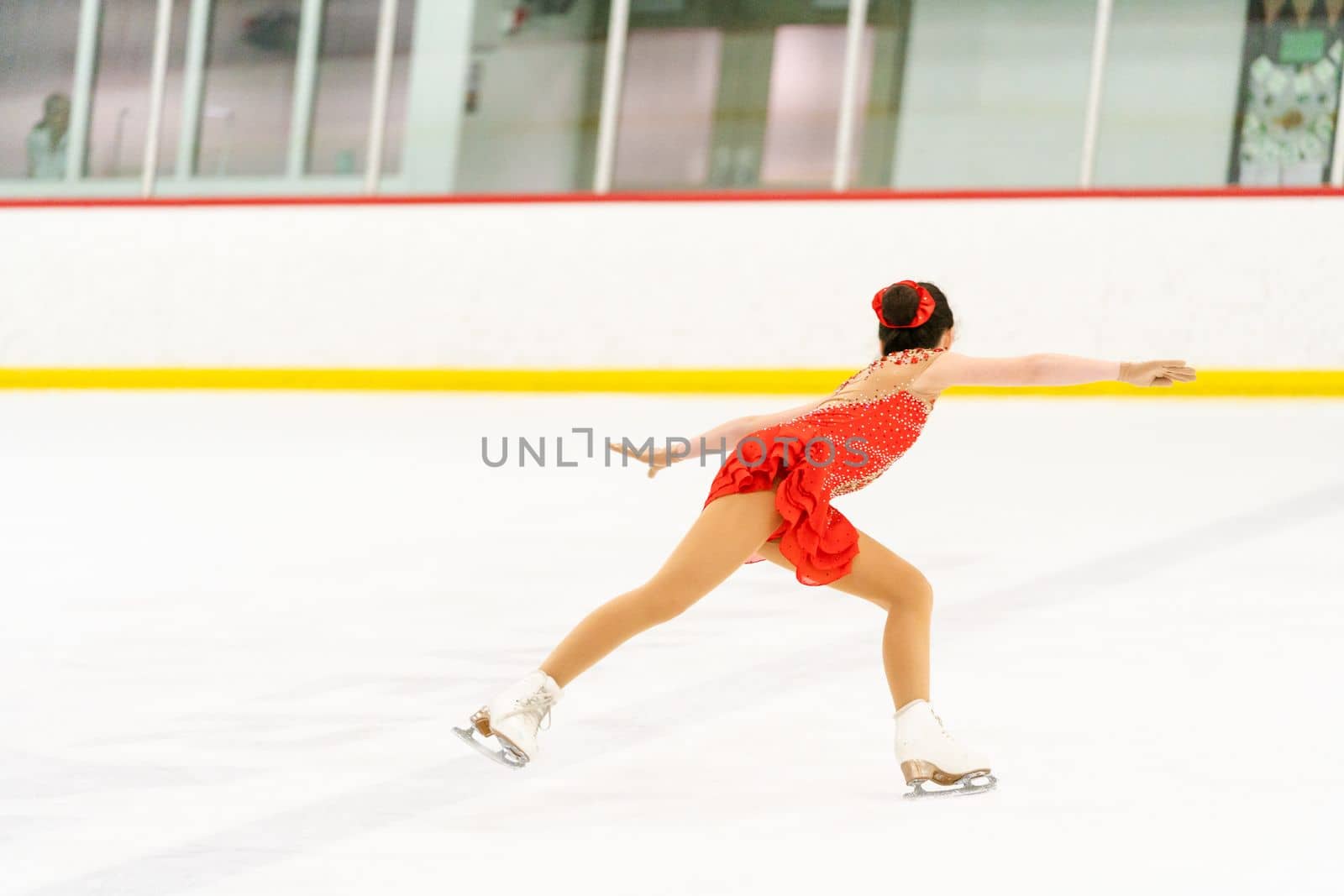 Teenage girl practicing figure skating on an indoor ice skating rink.