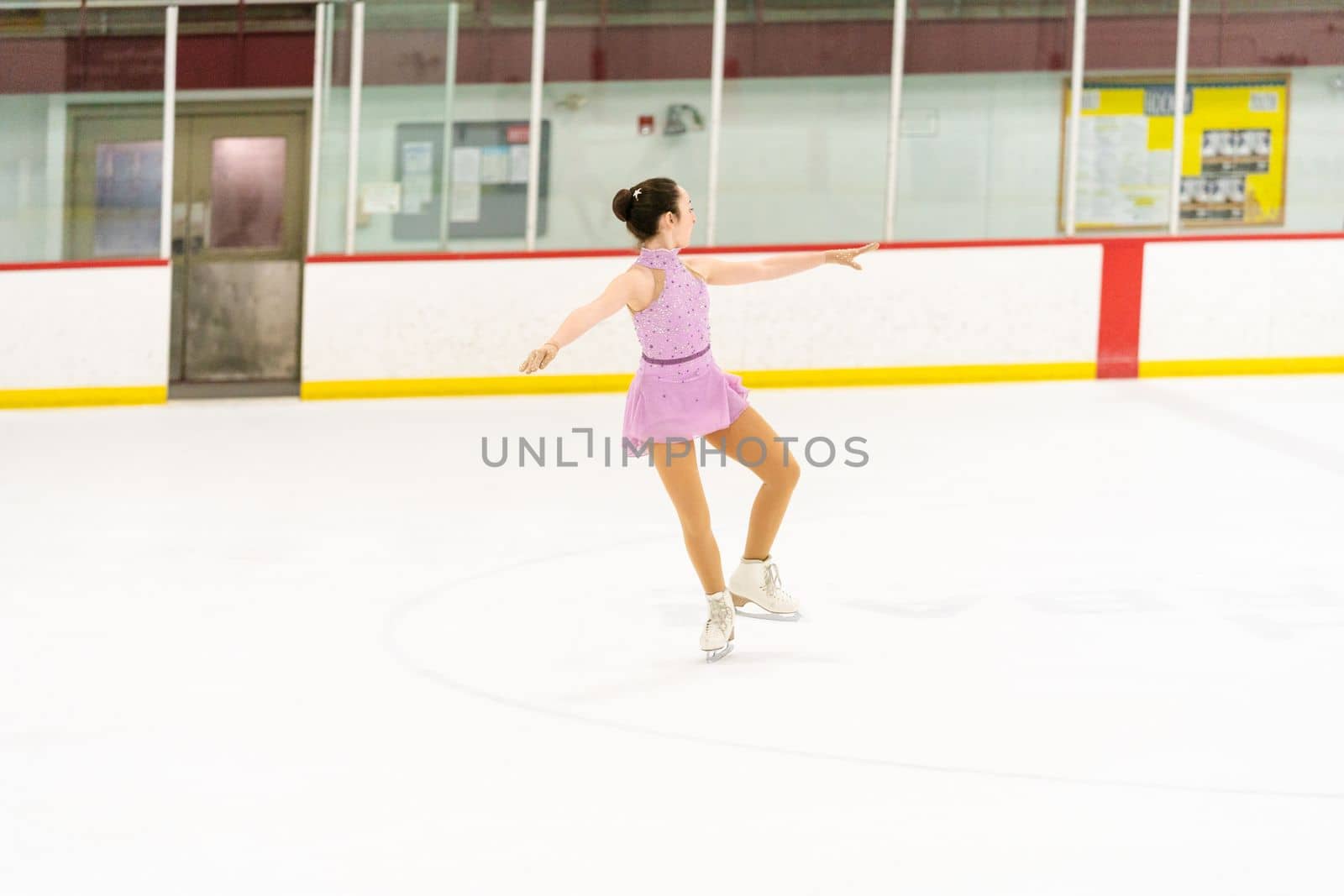 Teenage girl practicing figure skating on an indoor ice skating rink.